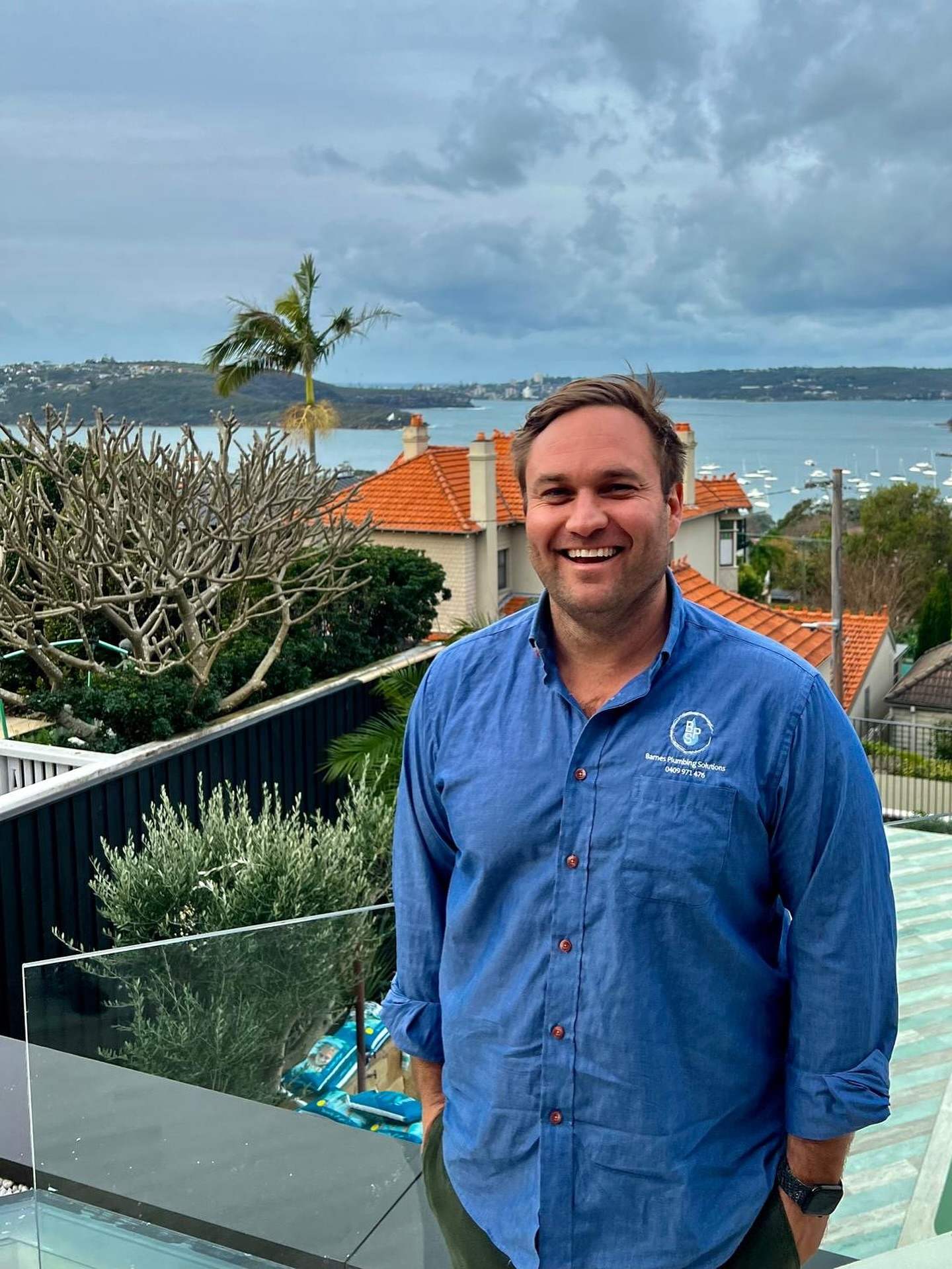 Jonathon Barnes, founder of Barnes Plumbing Solutions, in a blue work shirt with Sydney Harbour behind him