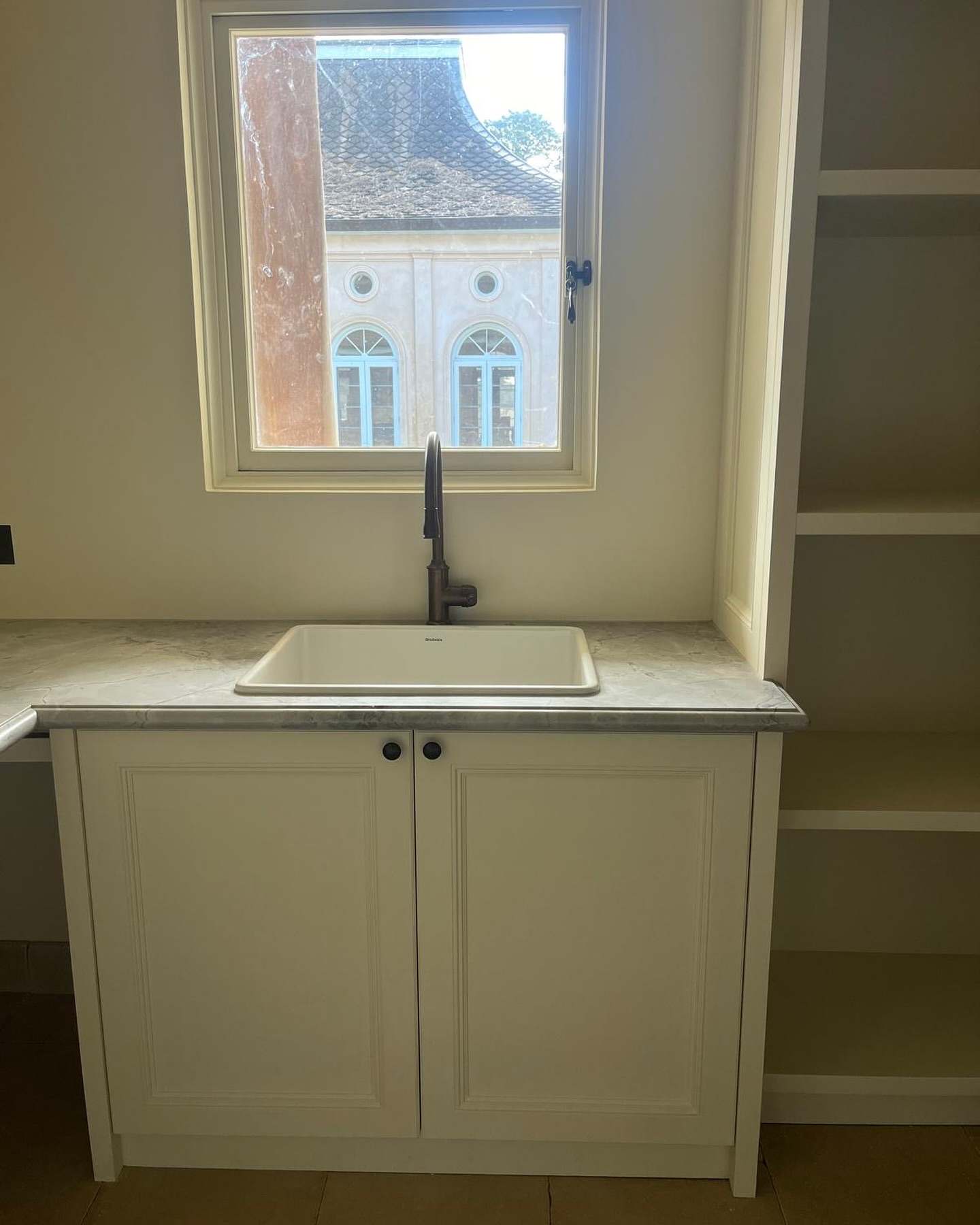 Laundry with a butler’s sink under an arched window, cream cabinetry and a matte black tap