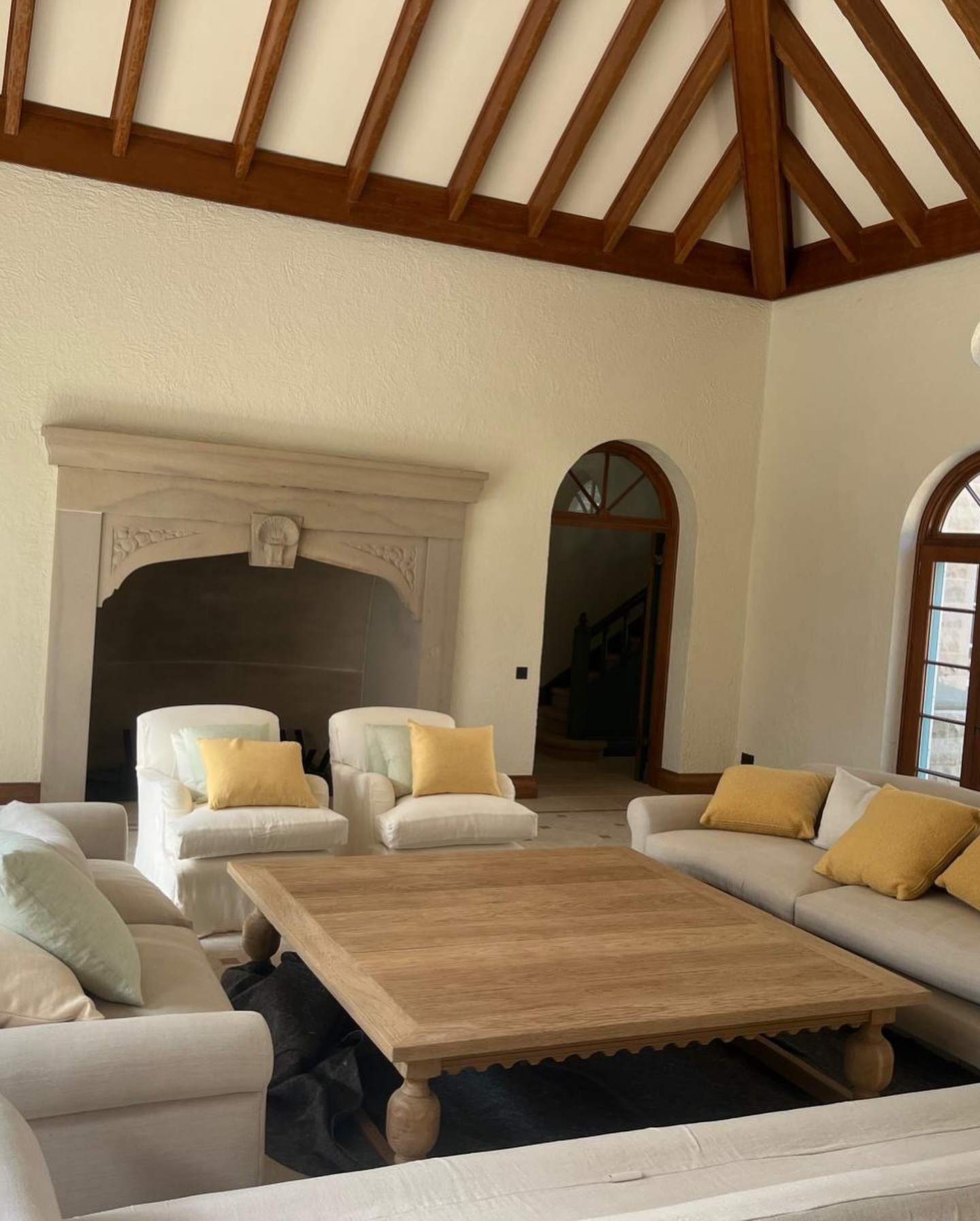 Finished living room of a heritage-style new build with exposed timber beams, stone fireplace and arched windows