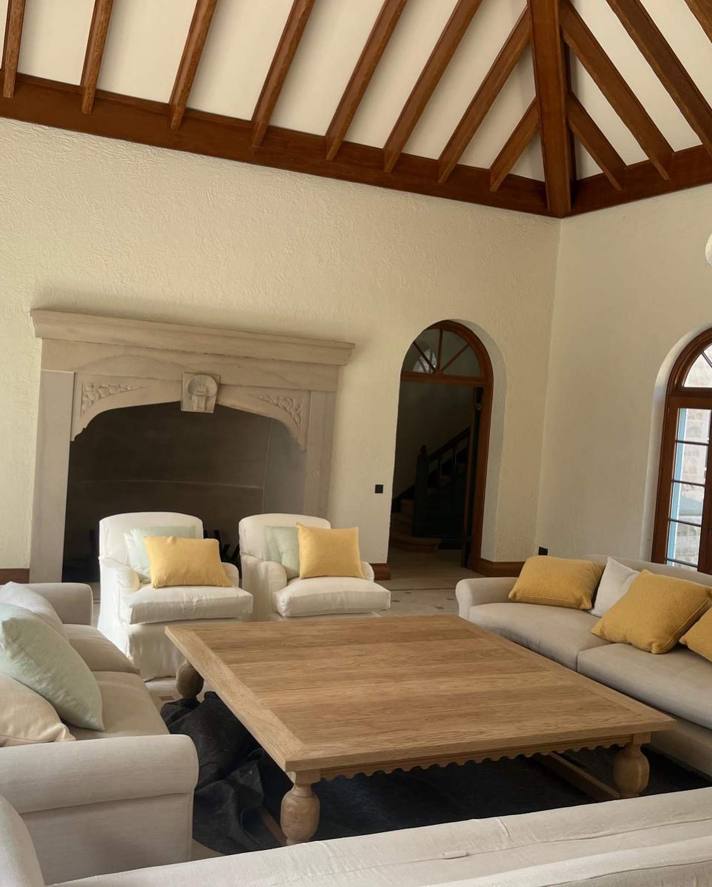 Finished living room of a new heritage-style house: exposed timber roof beams, stone fireplace and arched windows