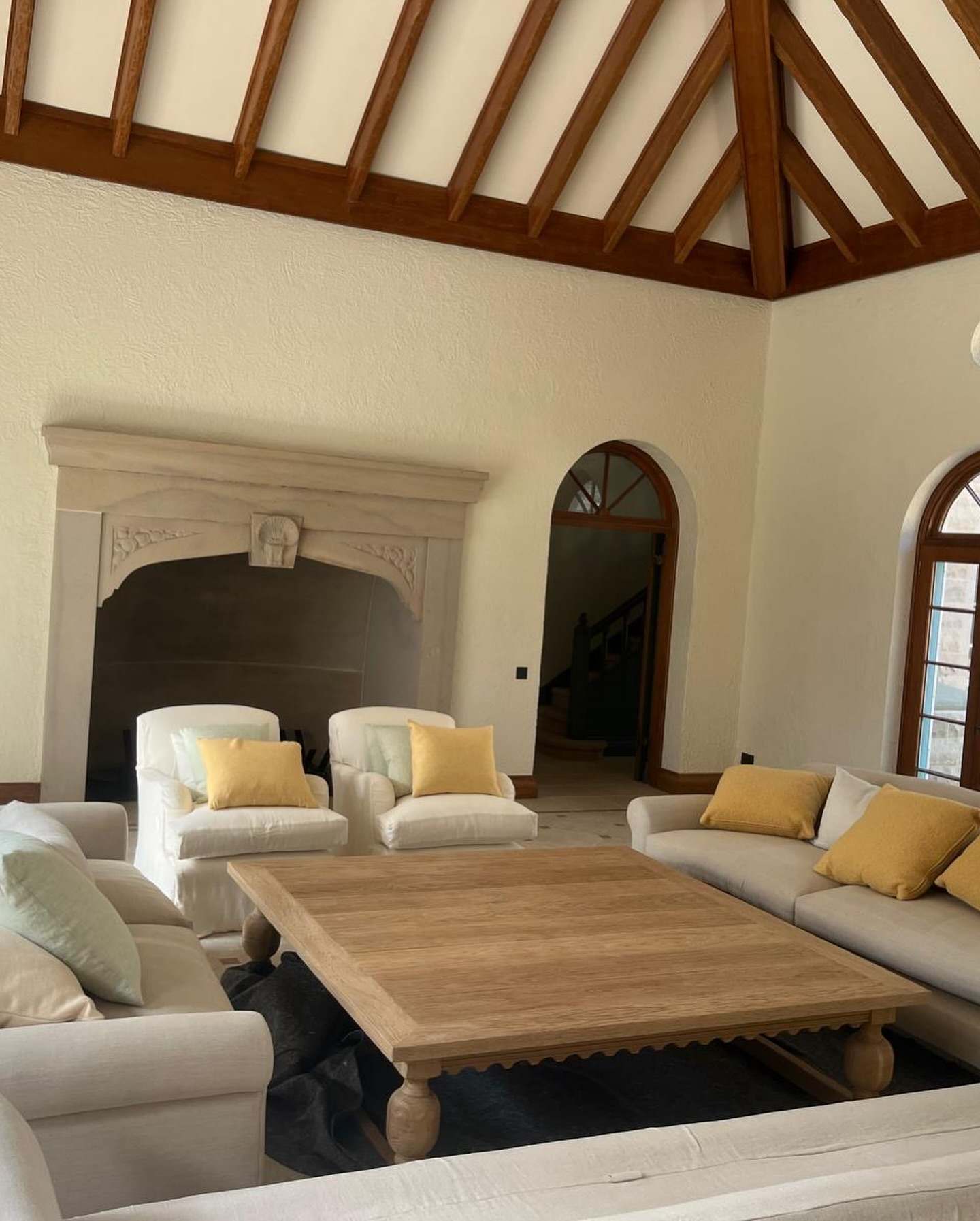 Finished living room of a new heritage-style house: exposed timber roof beams, stone fireplace and arched windows