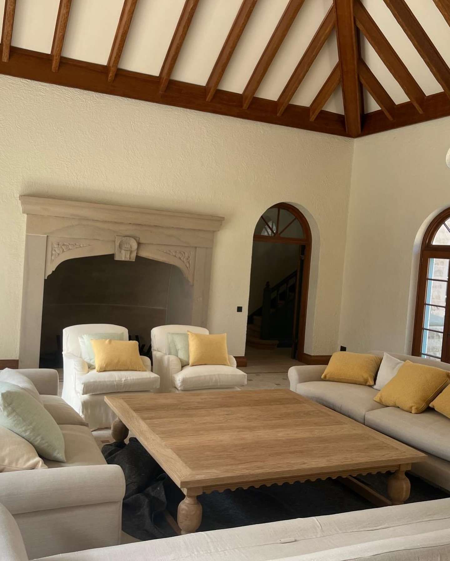 Finished living room of a heritage-style new build with exposed timber beams, stone fireplace and arched windows