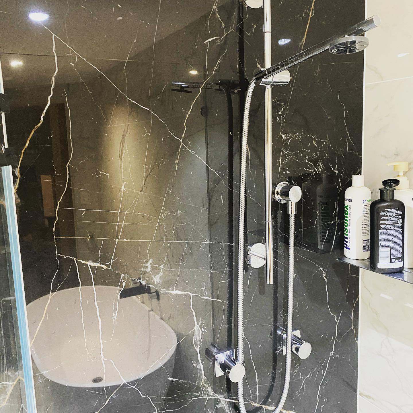 Walk-in shower clad in black marble with chrome fixtures and a freestanding bath