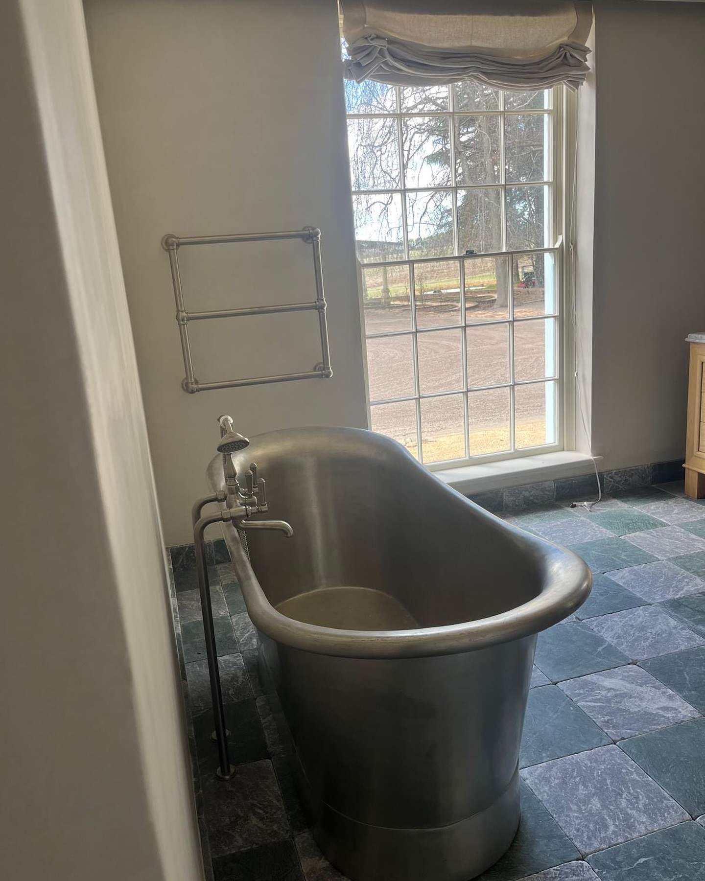 Freestanding metal bath under a tall window