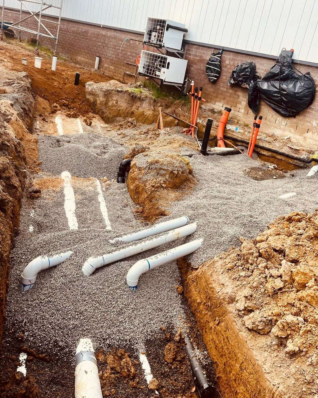 Stormwater pipes laid in gravel-bedded trenches beside a brick building