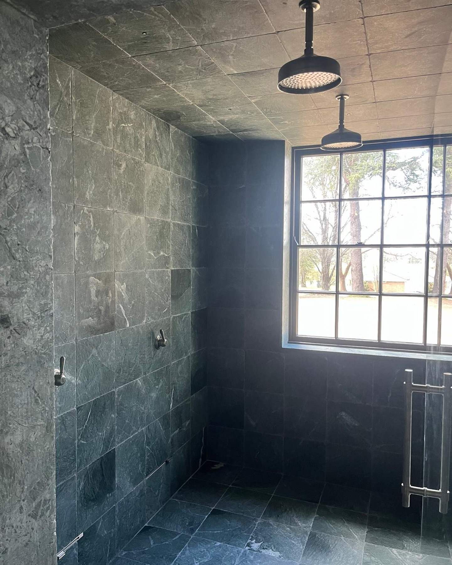Walk-in shower clad in dark stone with a black-framed window